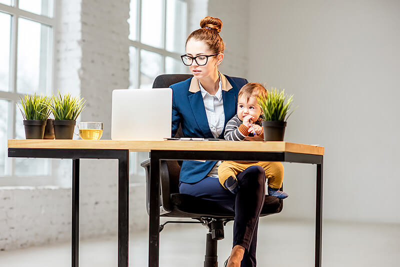 Woman wearing a suit holding her baby is working on the laptop
